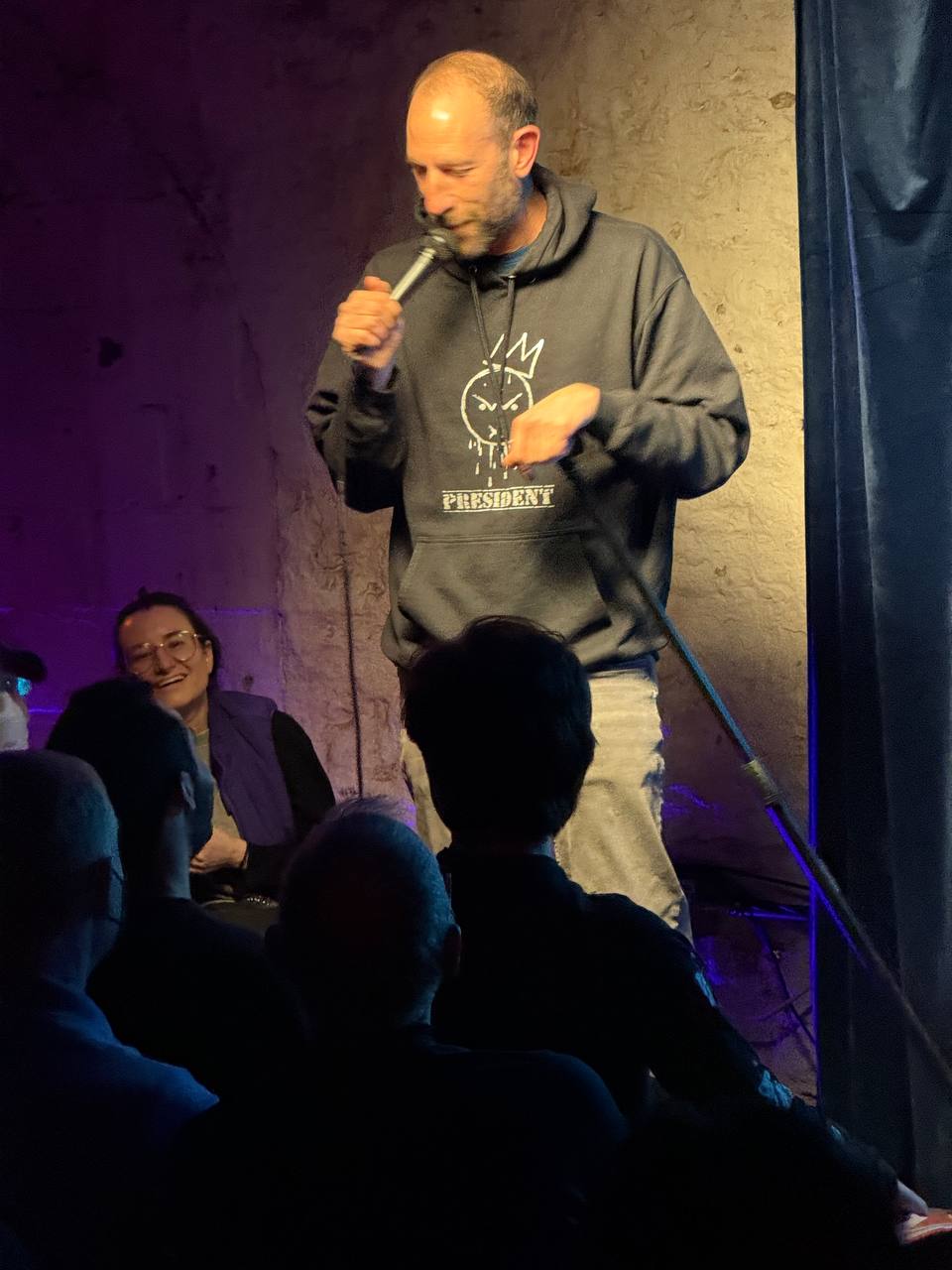 Comedian on stage under the SESH Comedy neon sign